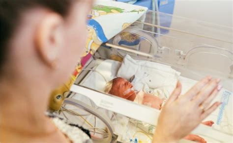 mama švelniai liečia neišnešiotą kūdikį inkubatoriuje