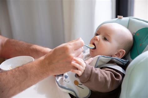 Kūdikis su seilinuku-apsiaustu valgo kietą maistą