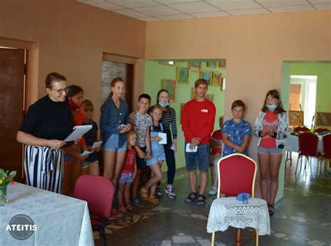 Įvairių etninės kilmės vaikų grupė sėdi prie bendro stalo ir mokosi kartu, vienas vaikas nešioja akinius, kitas - neįgaliojo vežimėlyje. Visi šypsosi.