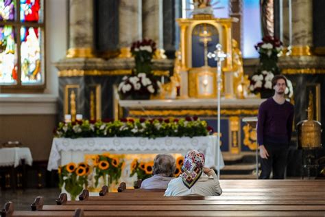 Žmonės susikaupę meldžiasi bažnyčioje, apšviestoje žvakių šviesa