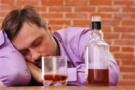 Jauno amžiaus asmuo, geriantis alkoholį vakarėlyje, fone - neryškūs žmonių siluetai