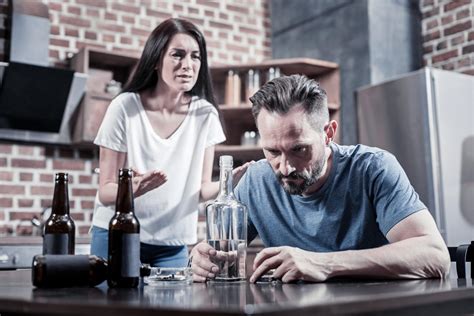 Alkoholizmas šeimoje: vaikas stebi tėvus, gaminančius maistą, ant stalo stovi alkoholio buteliai, tėvai atrodo nusiminę arba agresyvūs