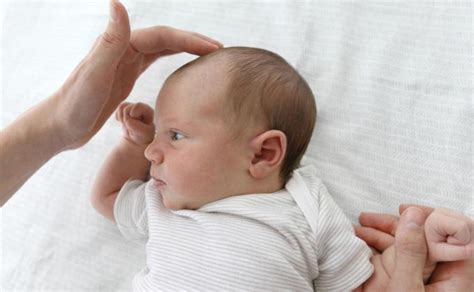 Mamos rankos švelniai liečia kūdikio galvą su luobele