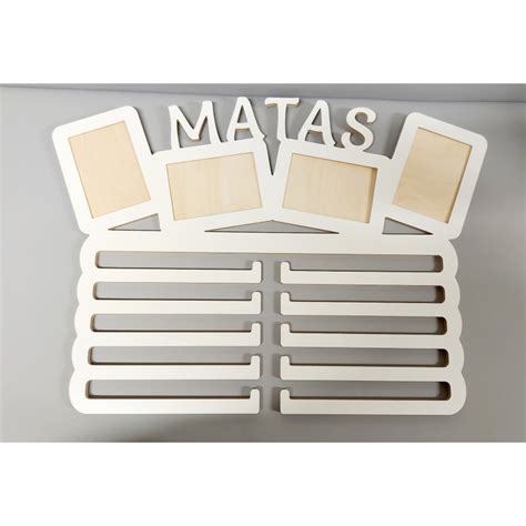 vaikas matuojasi ūgį prie medinės matuoklės su nuotraukų rėmeliais