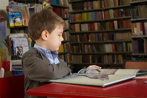 Vaikas skaitantis knygą bibliotekoje