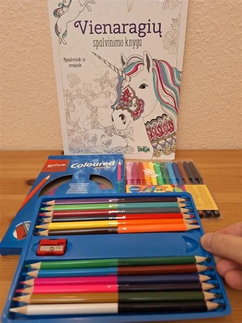 Vaikas, spalvinantis knygelę, su įvairiomis piešimo priemonėmis